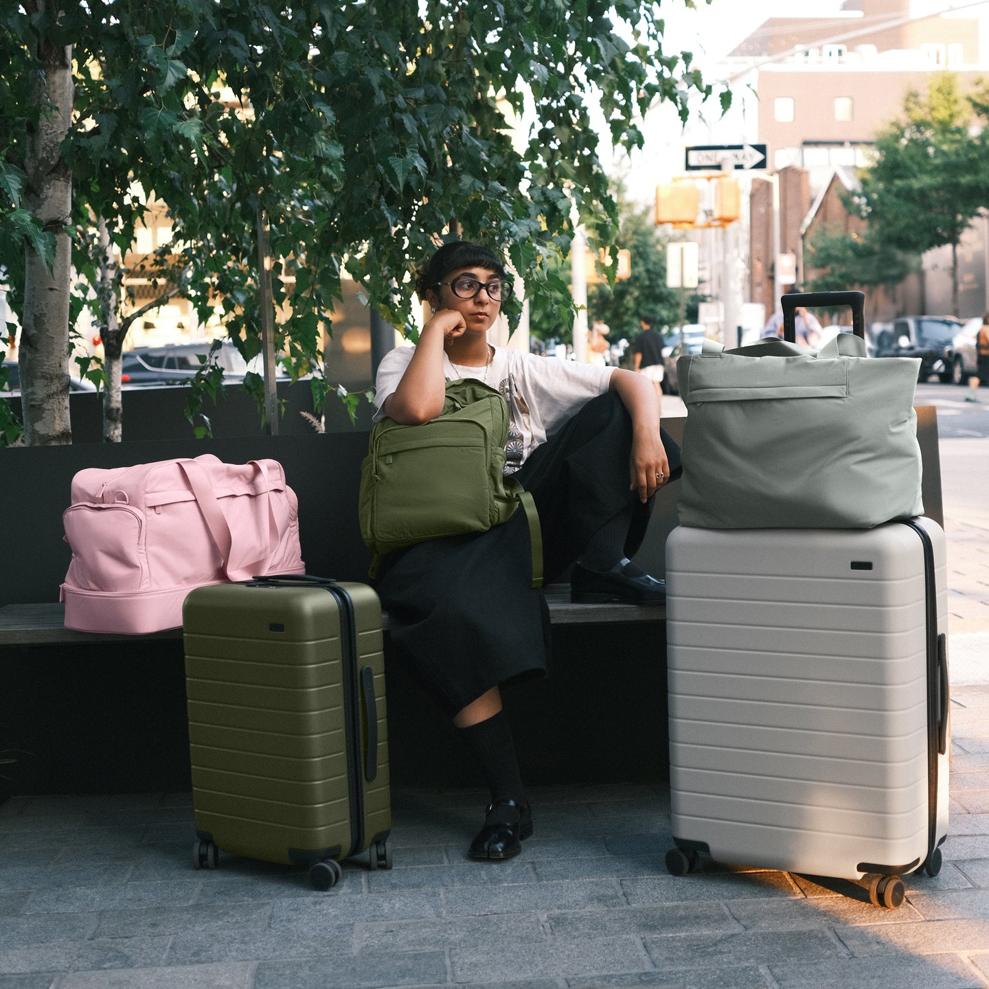 Female sitting in urban setting with Away The Bigger Carry-On, and The Large suitcases as well as Featherlight bags.