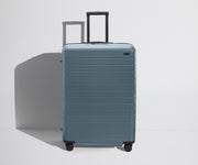 Front product view of The Large Flex suitcase in Coast Blue with raised handle