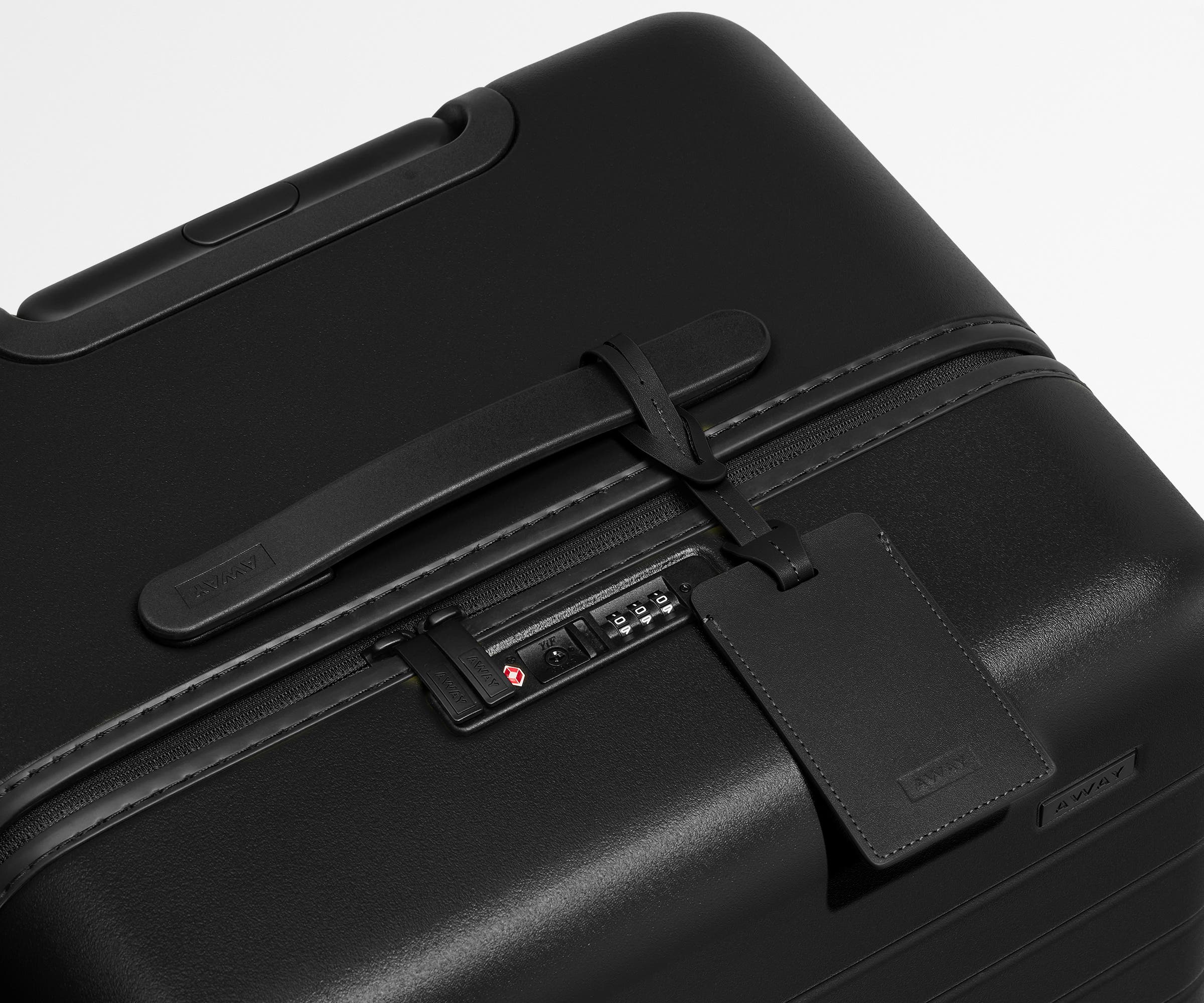 The Trunk suitcase in Jet Black shown shown from above highlighting TSA-approved combination lock and recycled leather luggage tag