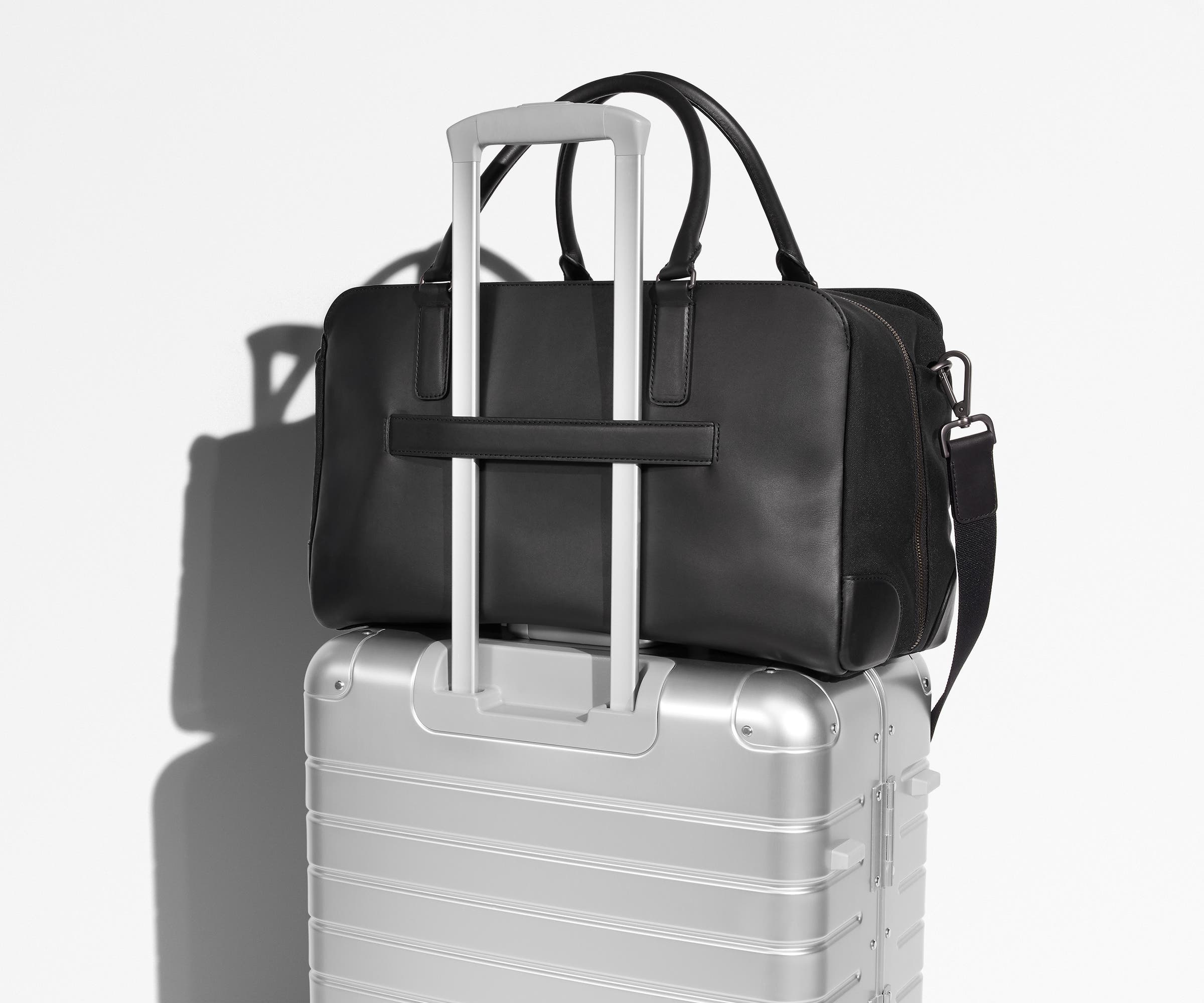 Transit Leather Duffle featured with a removable shoulder strap on top of an Aluminum suitcase