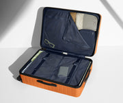The Large suitcase in Sorbet Orange shown open on its side and packed with Away's packing organizers to show capacity and the interior compression system, designed to help you pack more in