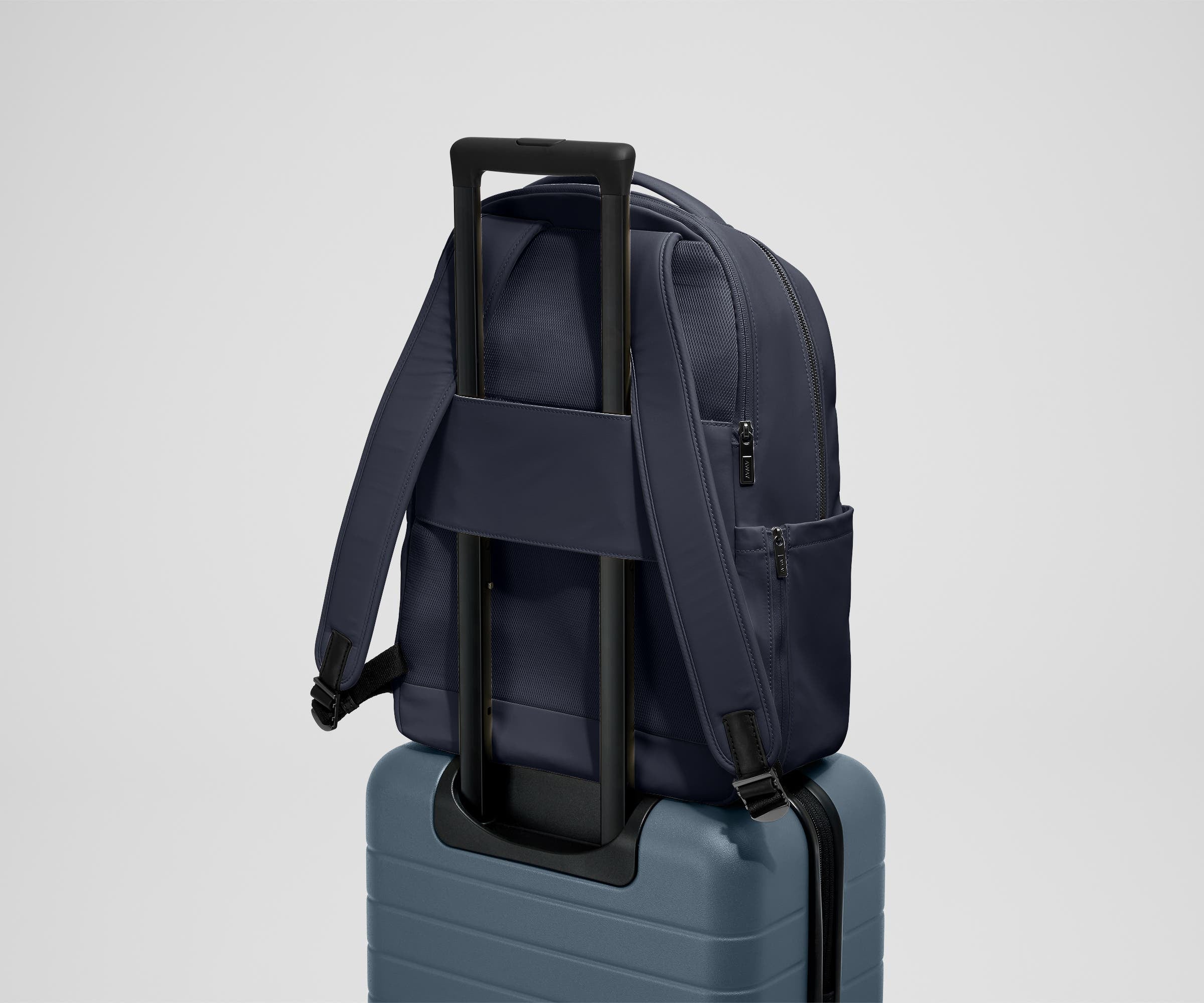 The Commuter Backpack on top of an Away suitcase, attached by the trolley pass-through sleeve
