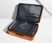 The Large Flex suitcase in Sorbet Orange shown open on its side and packed with Away's packing organizers to show capacity and the interior compression system, designed to help you pack more in