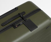 The Medium suitcase in Olive Green shown shown from above highlighting TSA-approved combination lock and recycled leather luggage tag