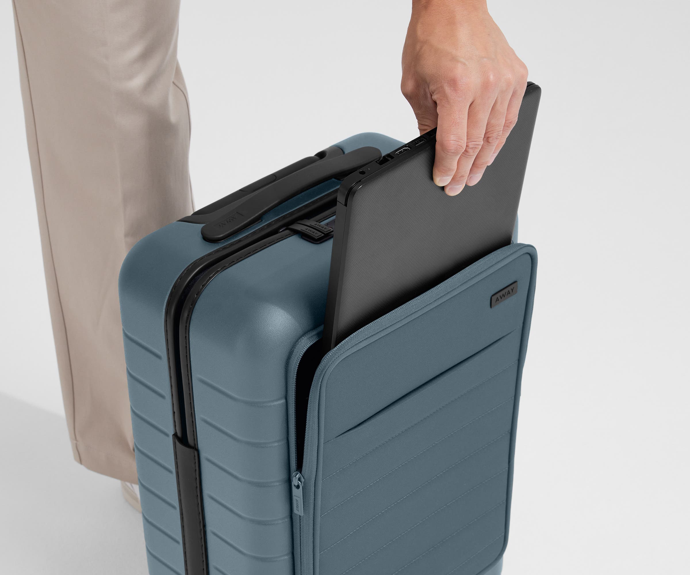 Zoomed in shot of talent slipping a laptop into the front pocket of The Front Pocket Carry-On in Coast Blue