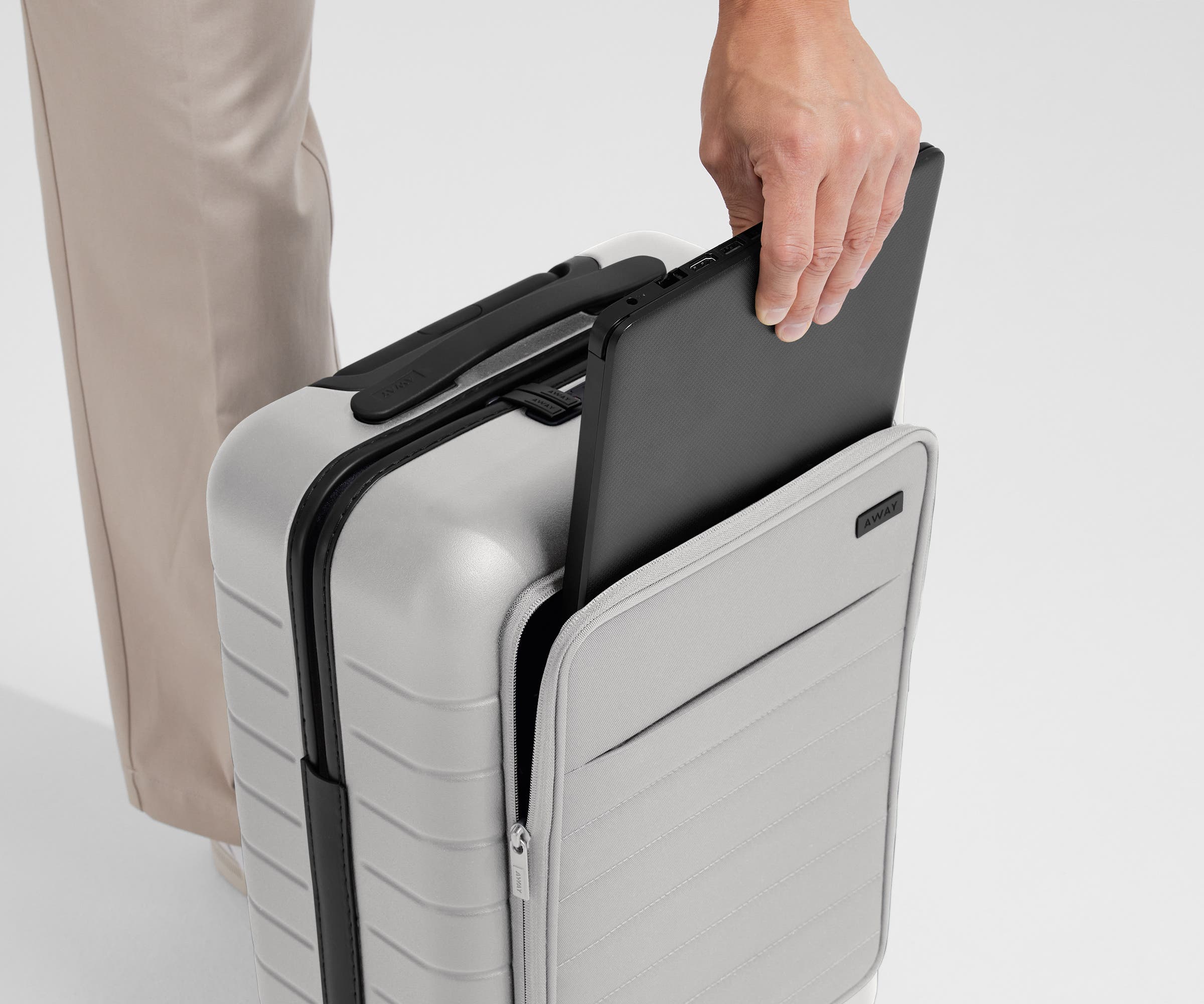 Zoomed in shot of talent slipping a laptop into the front pocket of The Front Pocket Carry-On in Cloud Gray