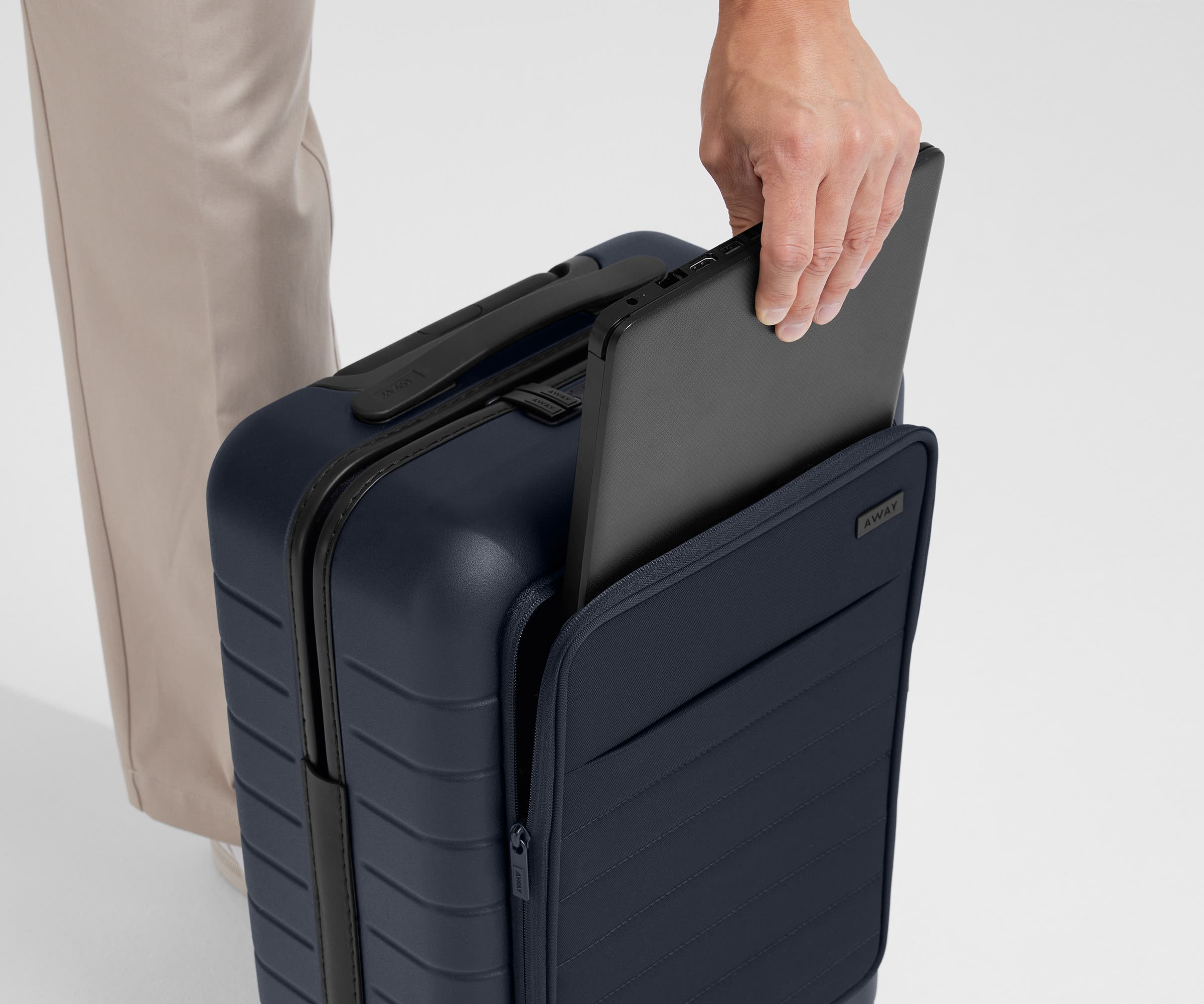 Zoomed in shot of talent slipping a laptop into the front pocket of The Front Pocket Carry-On in Navy Blue
