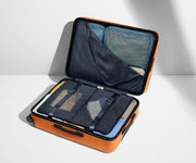 The Medium suitcase in Sorbet Orange shown open on its side and packed with Away's packing organizers to show capacity and the interior compression system, designed to help you pack more in