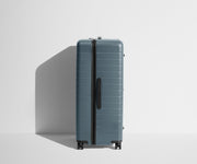 Side product view of The Trunk suitcase in Coast Blue to show the slimmer top lid and deeper main compartment for easy access and packing