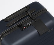 The Carry-On suitcase in Navy Blue shown shown from above highlighting TSA-approved combination lock and recycled leather luggage tag