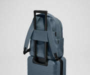 The Commuter Backpack on top of an Away suitcase, attached by the trolley pass-through sleeve