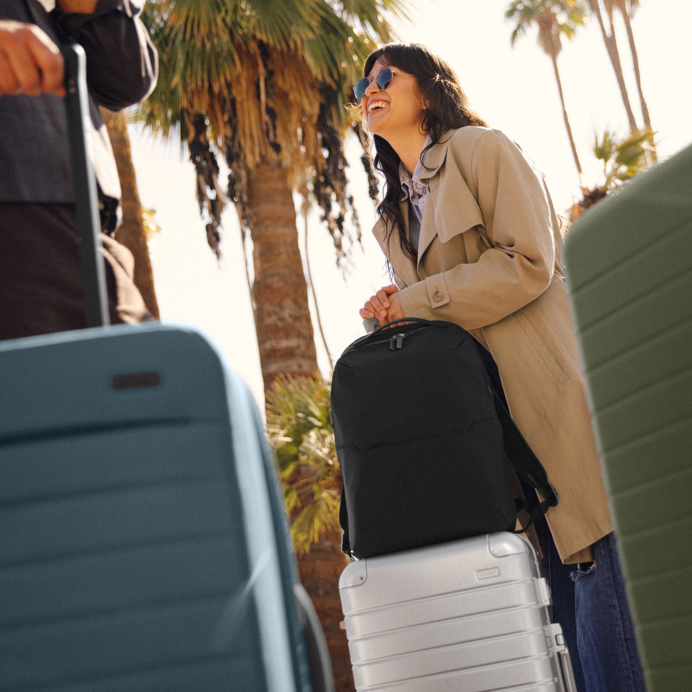 Person traveling with multiple suitcases and an Away backpack in front of a palm tree