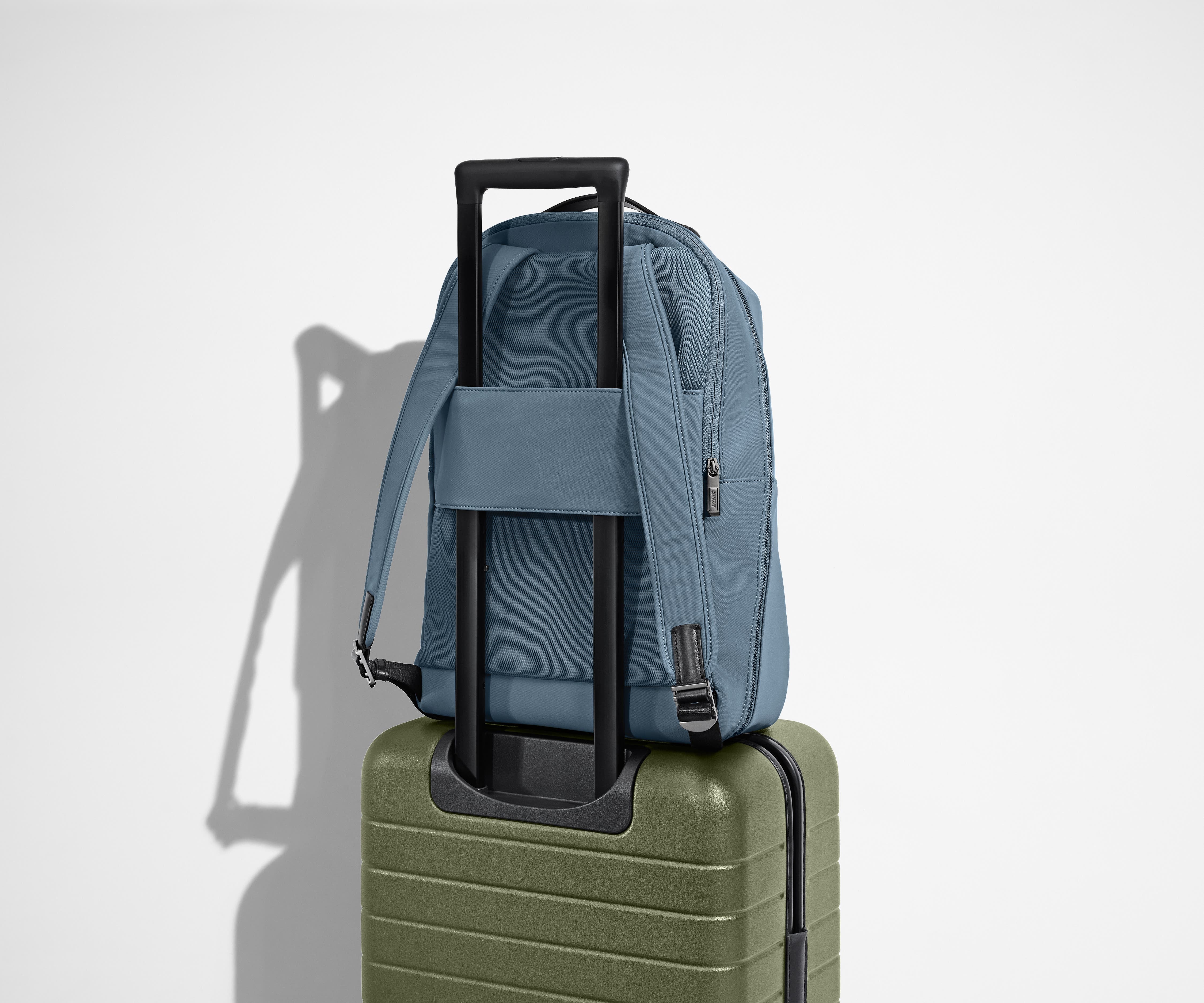 The Everywhere Zip Backpack in Coast Blue sitting on an Away Carry-On suitcase