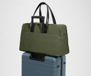 Green travel bag on top of a suitcase against a light gray background