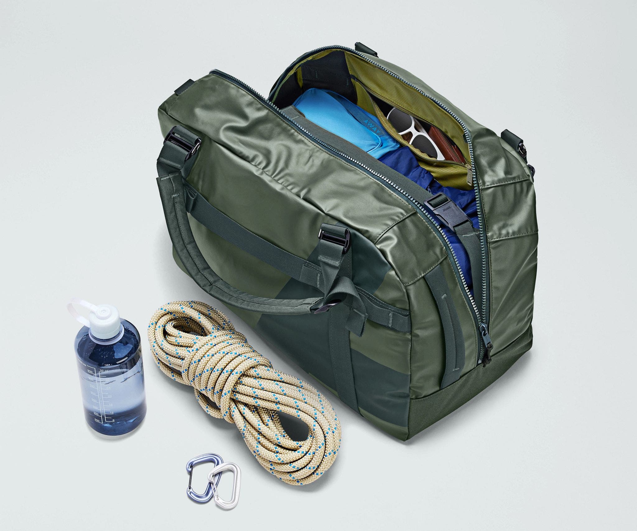 Active Duffle 55L packed with travel essentials and outdoor gear including a packing cube, sunglasses, wallet, carabiner and rope, and water bottle