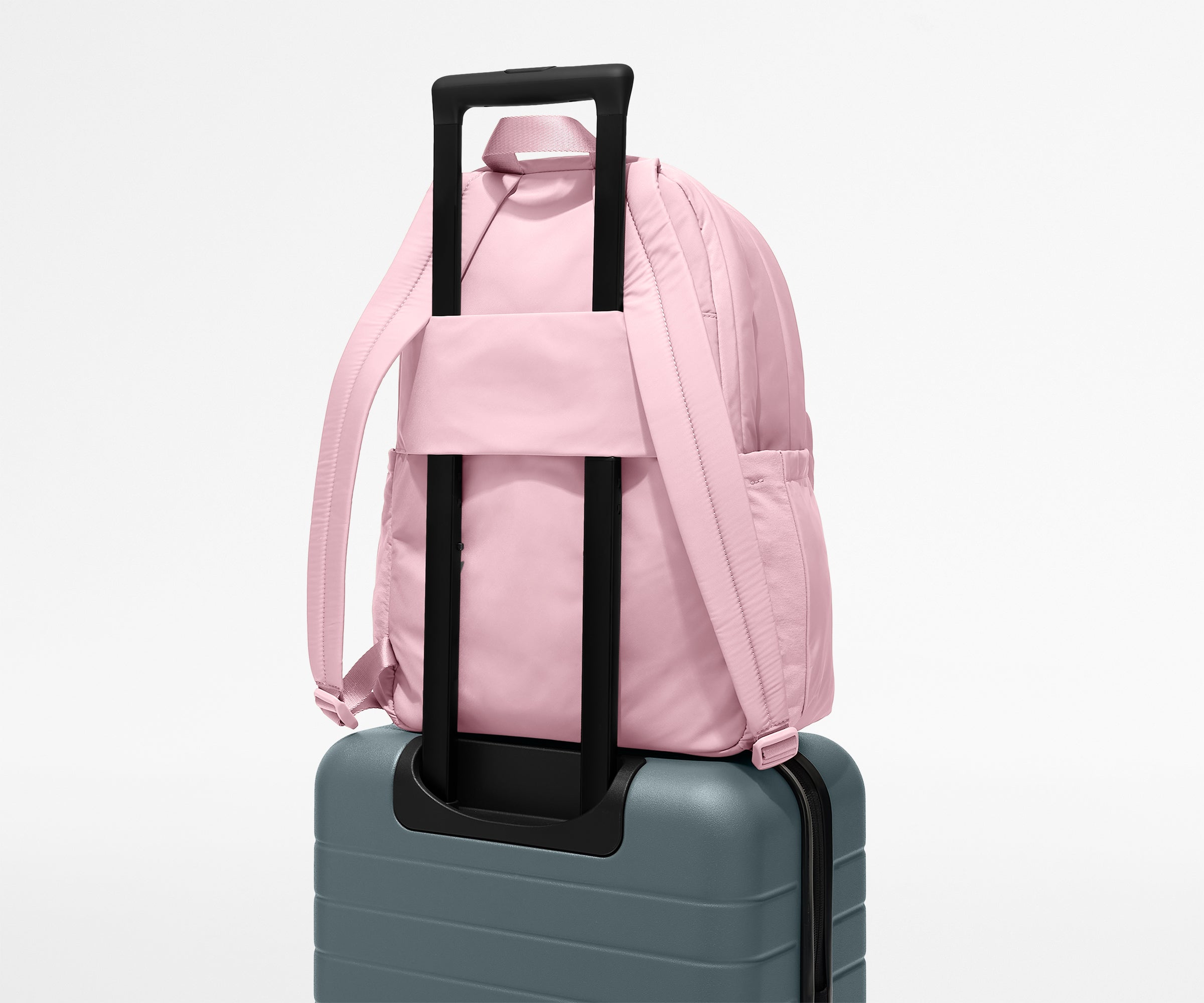 Pink backpack with black handle on a gray suitcase against a white background