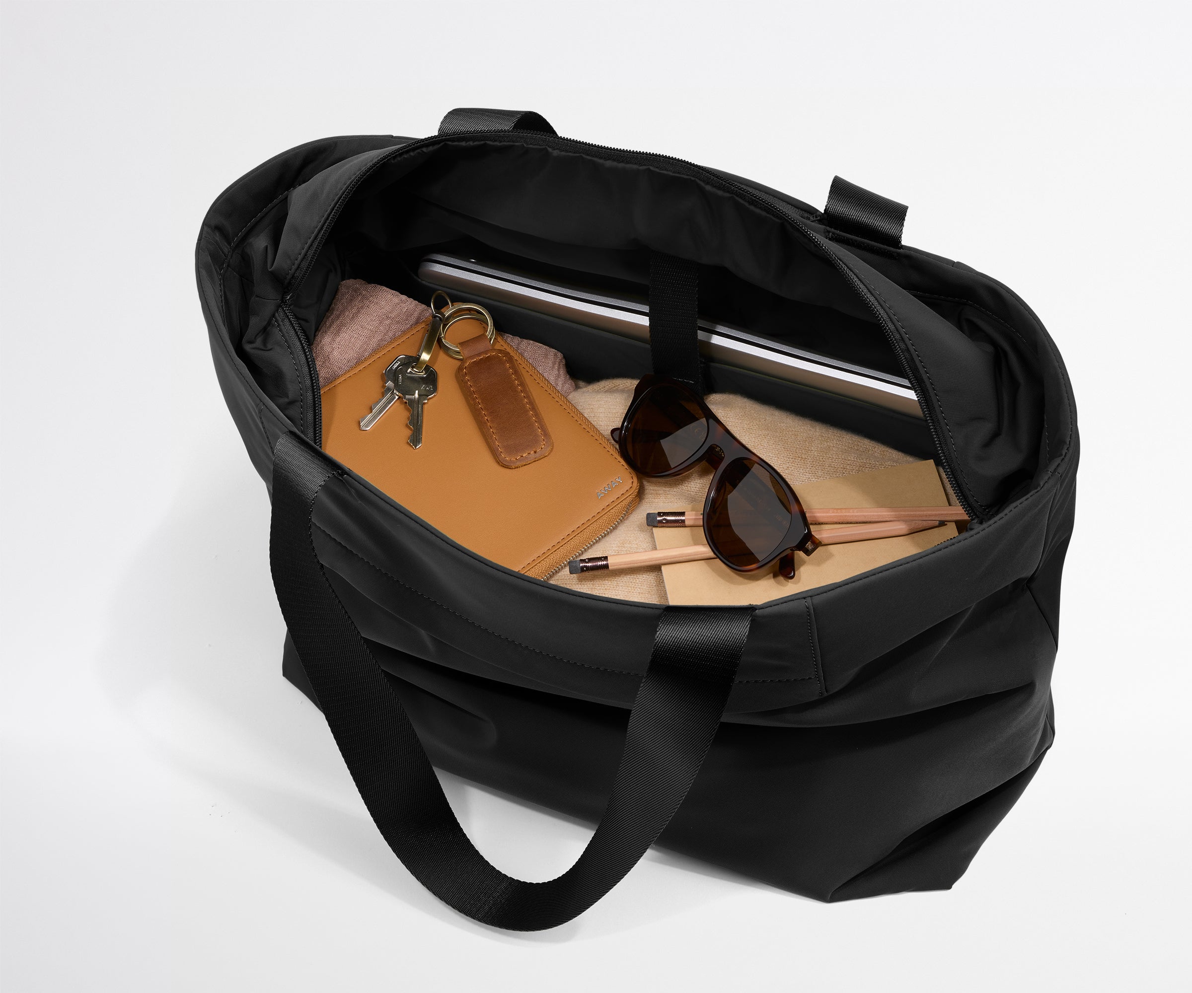 Black duffel bag with items like a notebook, keys, and sunglasses on a light gray background