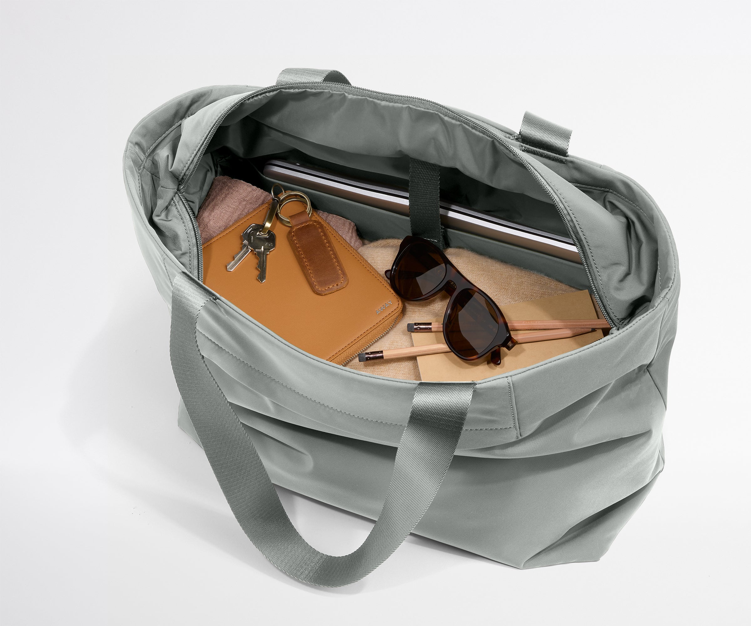 Gray duffel bag with items like a notebook, sunglasses, and keys on a light gray background