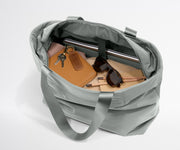Gray duffel bag with items like a notebook, sunglasses, and keys on a light gray background