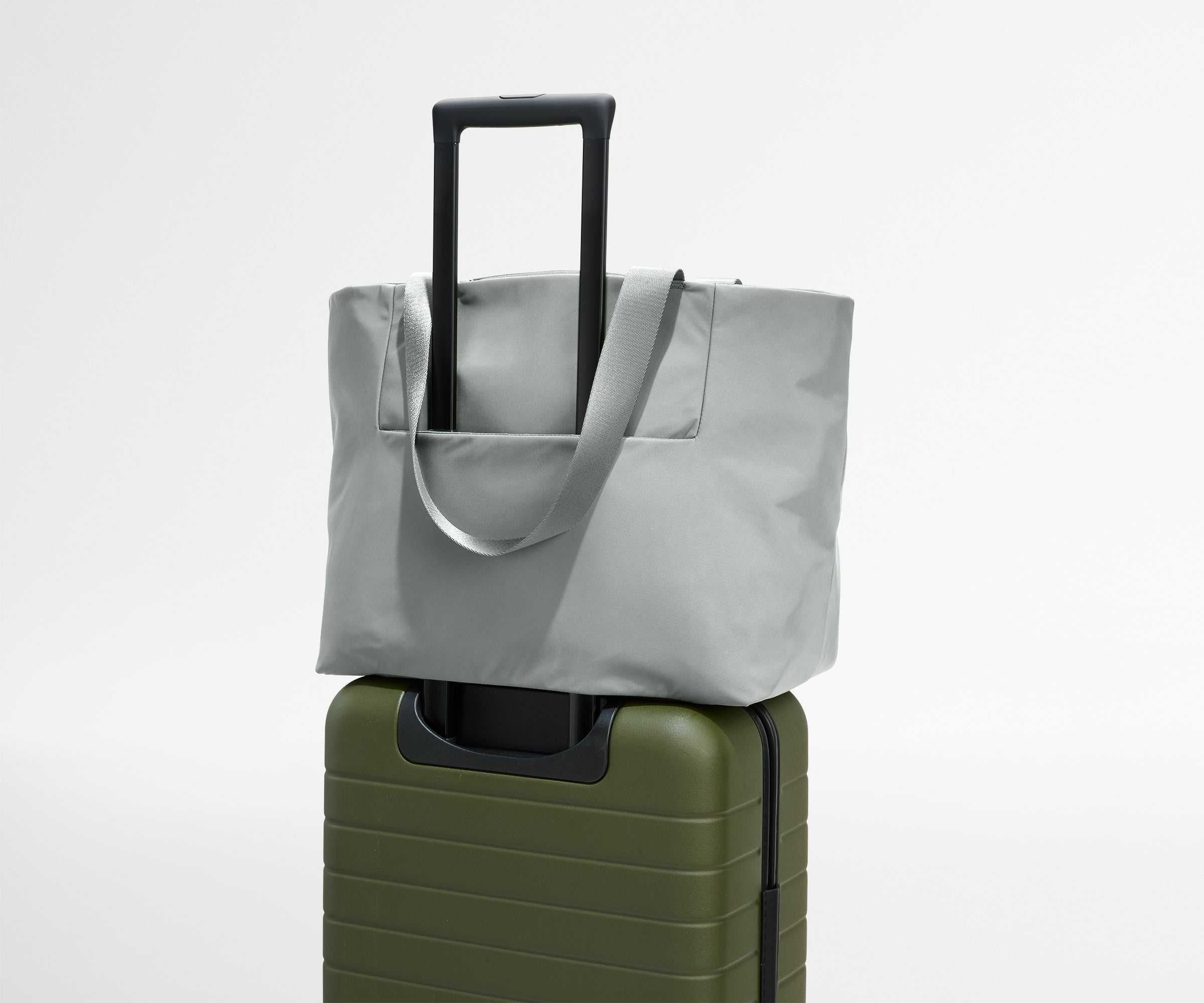 Gray tote bag on top of a green suitcase against a white background