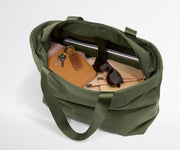 Green bag with items like a notebook, keys, and sunglasses on a white background