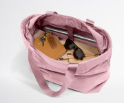 Pink tote bag with items like a notebook, sunglasses, and keys on a light gray background