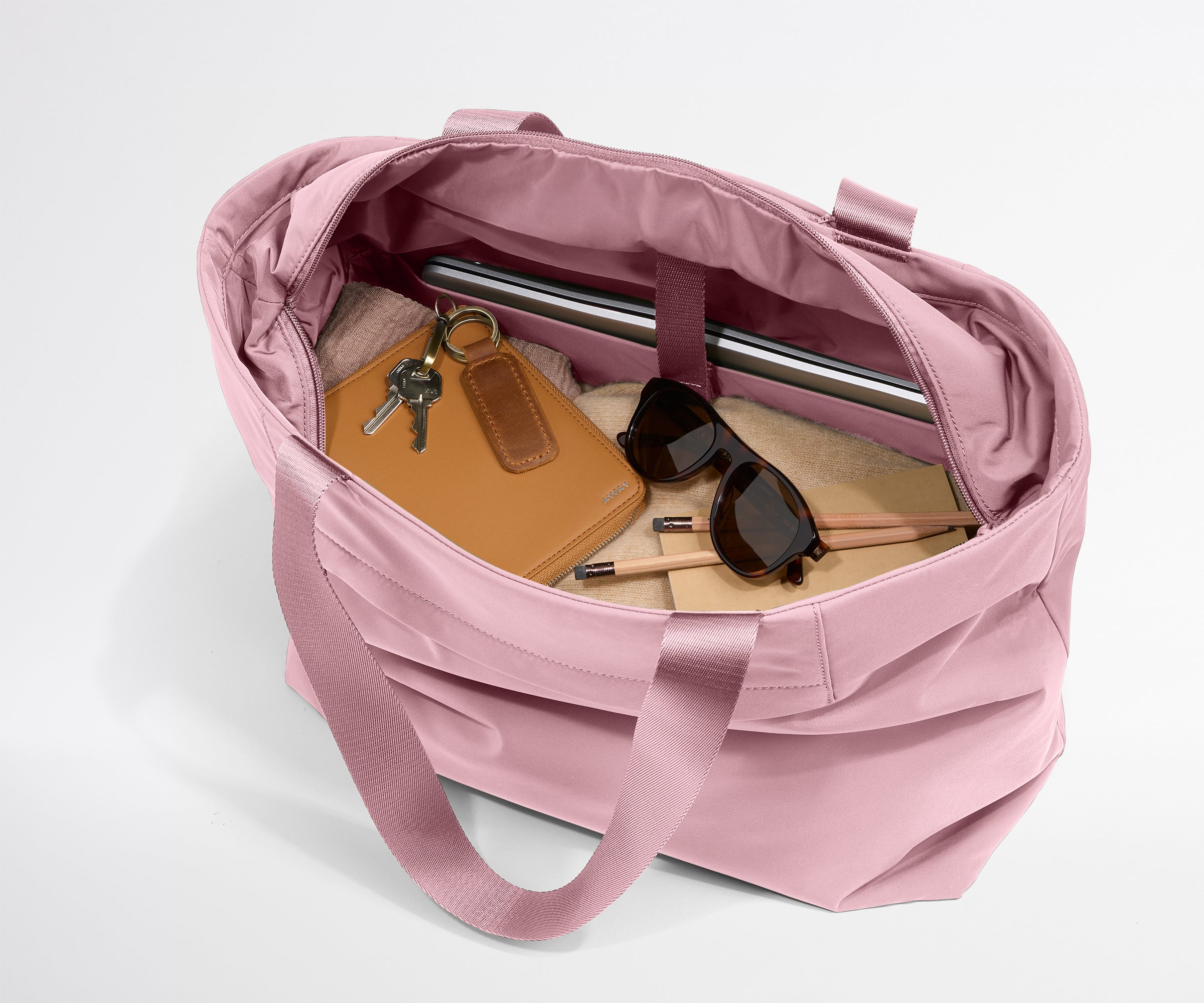 Pink tote bag with items like a notebook, sunglasses, and keys on a light gray background