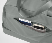 Gray duffel bag with a pocket containing a passport and phone on a light gray background