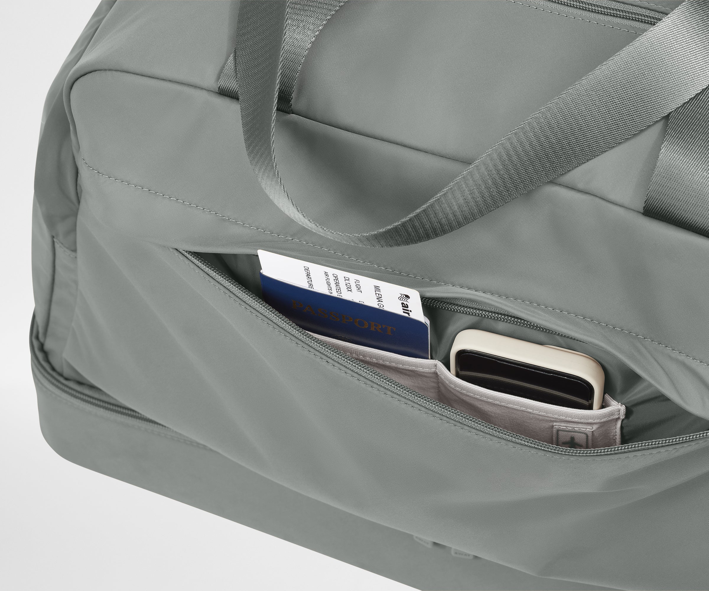 Gray duffel bag with a pocket containing a passport and phone on a light gray background