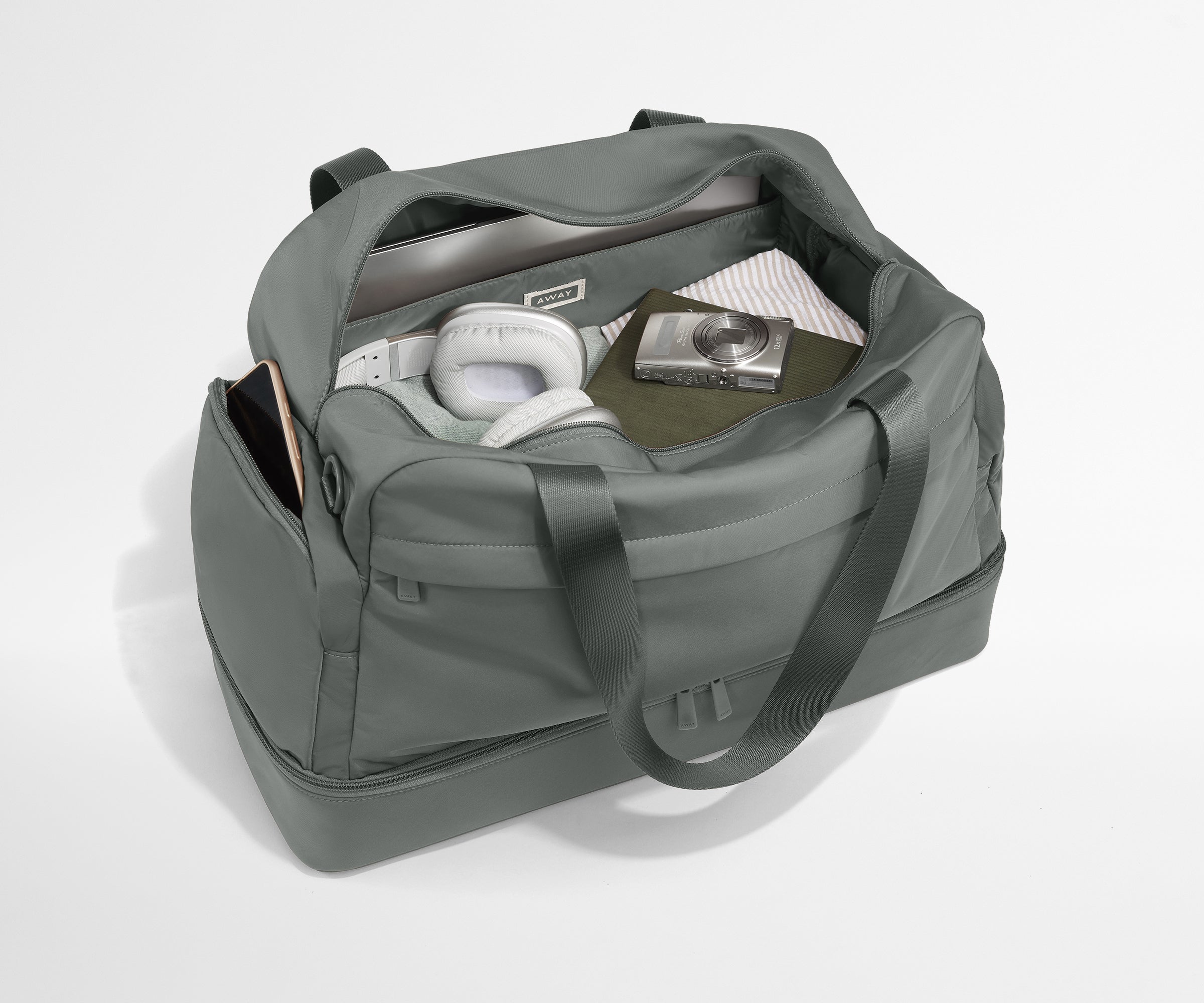 Gray duffel bag with items including a phone, headphones, and a book on a white background