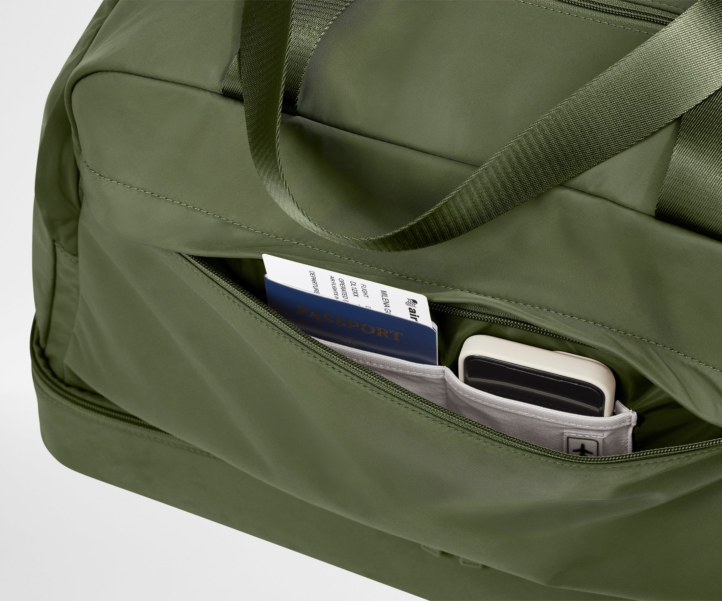 Green duffel bag with a pocket containing a passport and phone on a light gray background