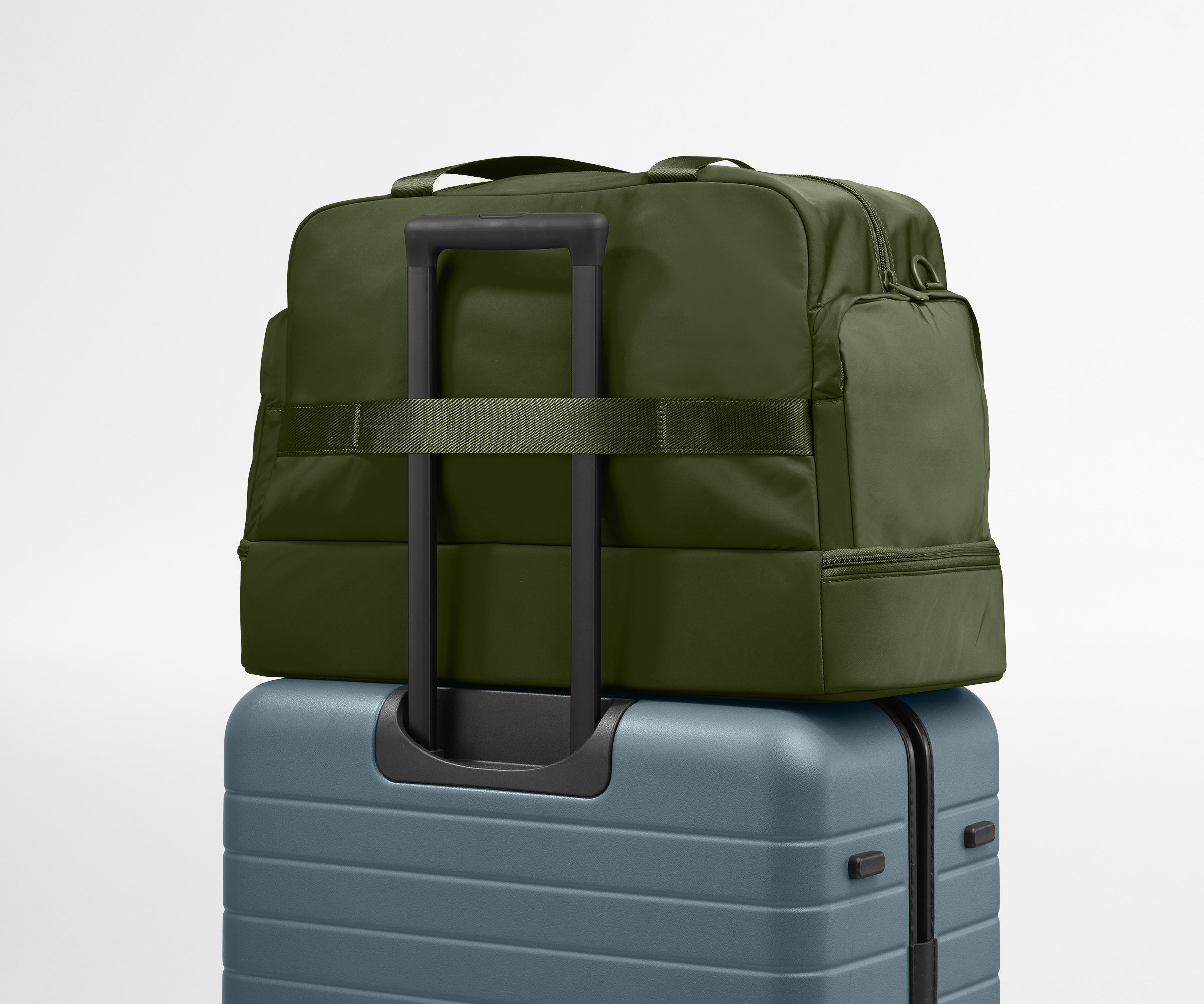 Green travel bag with wheels on top of a blue suitcase against a light gray background