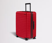 Red suitcase with black handle and wheels on a light gray background