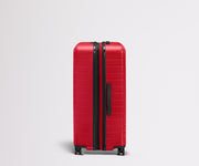 Red suitcase with black handle and wheels on a light gray background