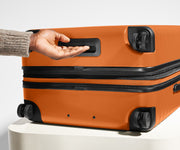 The Medium Flex suitcase in Sorbet Orange shown from below highlighting the underside grab handle