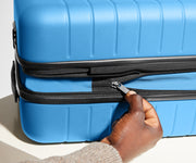 A model unzipping the wraparound zipper to expand the Flex suitcase in Splash Blue and create more packing space