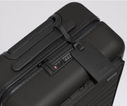 The Front Pocket Carry-On suitcase in Jet Black shown shown from above highlighting TSA-approved combination lock and black leather luggage tag