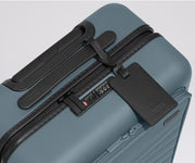 The Front Pocket Carry-On suitcase in Coast Blue shown shown from above highlighting TSA-approved combination lock and black leather luggage tag
