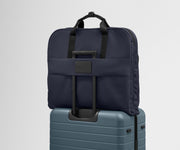 The trolley sleeve on the back of the Garment Bag in Navy Blue slides over the trolley handle of an Away Medium suitcase in Coast Blue to make travel seamless