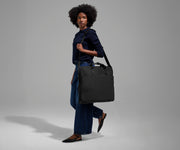 A female model carrying the Garment Bag in Jet Black over her shoulder using the adjustable, removable shoulder strap