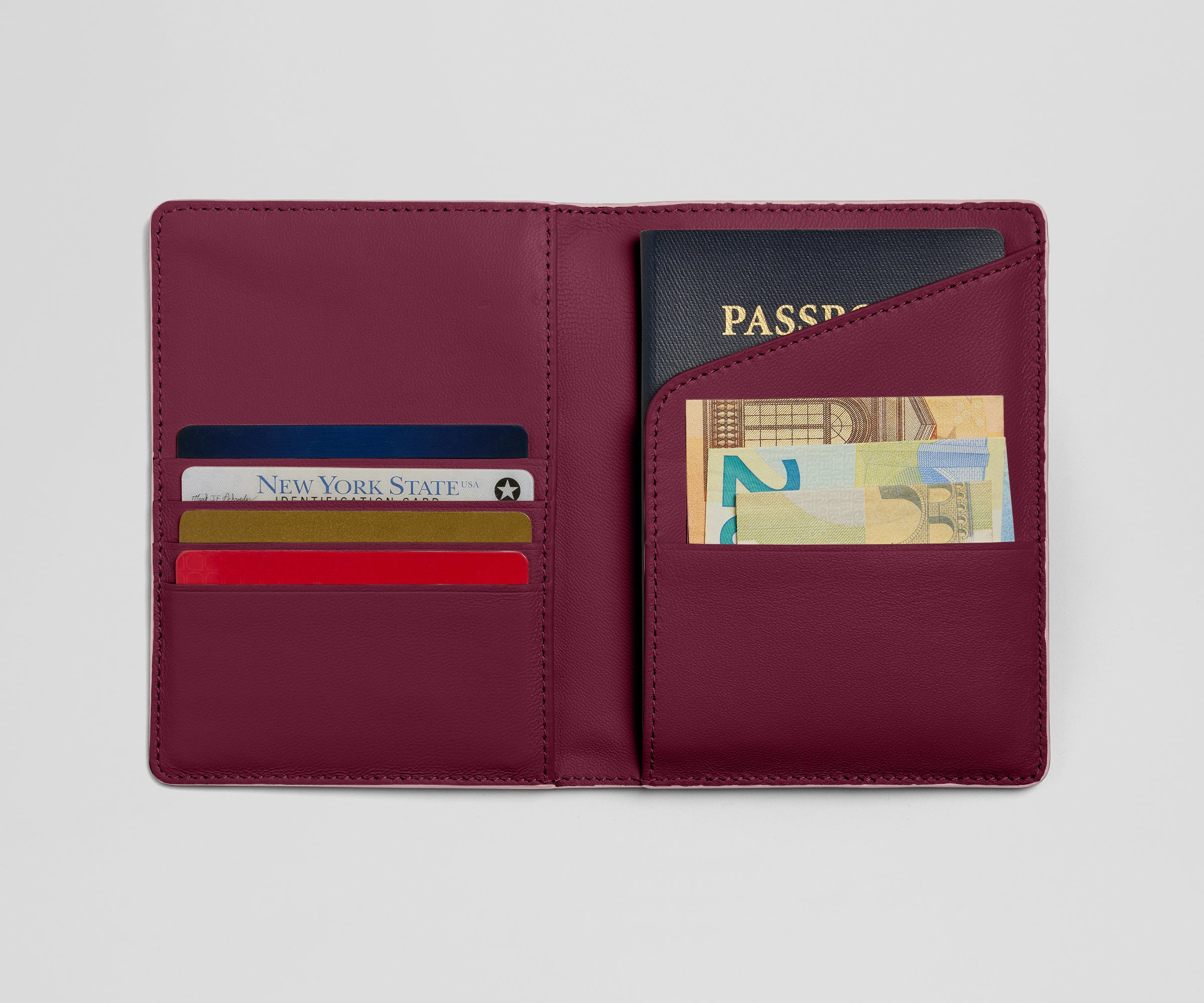 Maroon leather wallet with card slots and a passport holder on a light gray background