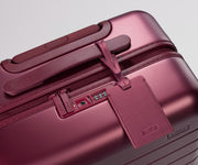 Maroon suitcase with a luggage tag on a light gray background