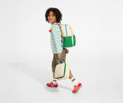 A child model wearing the Kids Backpack in Marshmallow White with the chest strap in use and holds the Kids Lunch Box in Marshmallow White
