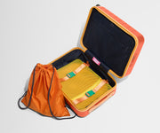 The Kids Carry-On suitcase in Poppy Orange shown open and empty on its side to show capacity, and an orange laundry bag can double as a backpack for smaller travelers.