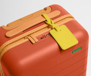 The Kids Carry-On suitcase in Poppy Orange shown shown from above highlighting TSA-approved combination lock and color-blocked silicone luggage tag
