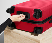 Red suitcase with a hand reaching to open it on a light wooden surface.