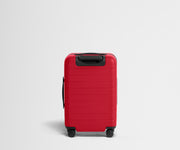 Red suitcase with black handle and wheels on a light gray background
