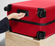 Red suitcase with a hand on the handle against a neutral background
