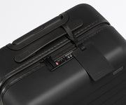 The Carry-On suitcase in Jet Black shown shown from above highlighting TSA-approved combination lock and recycled leather luggage tag