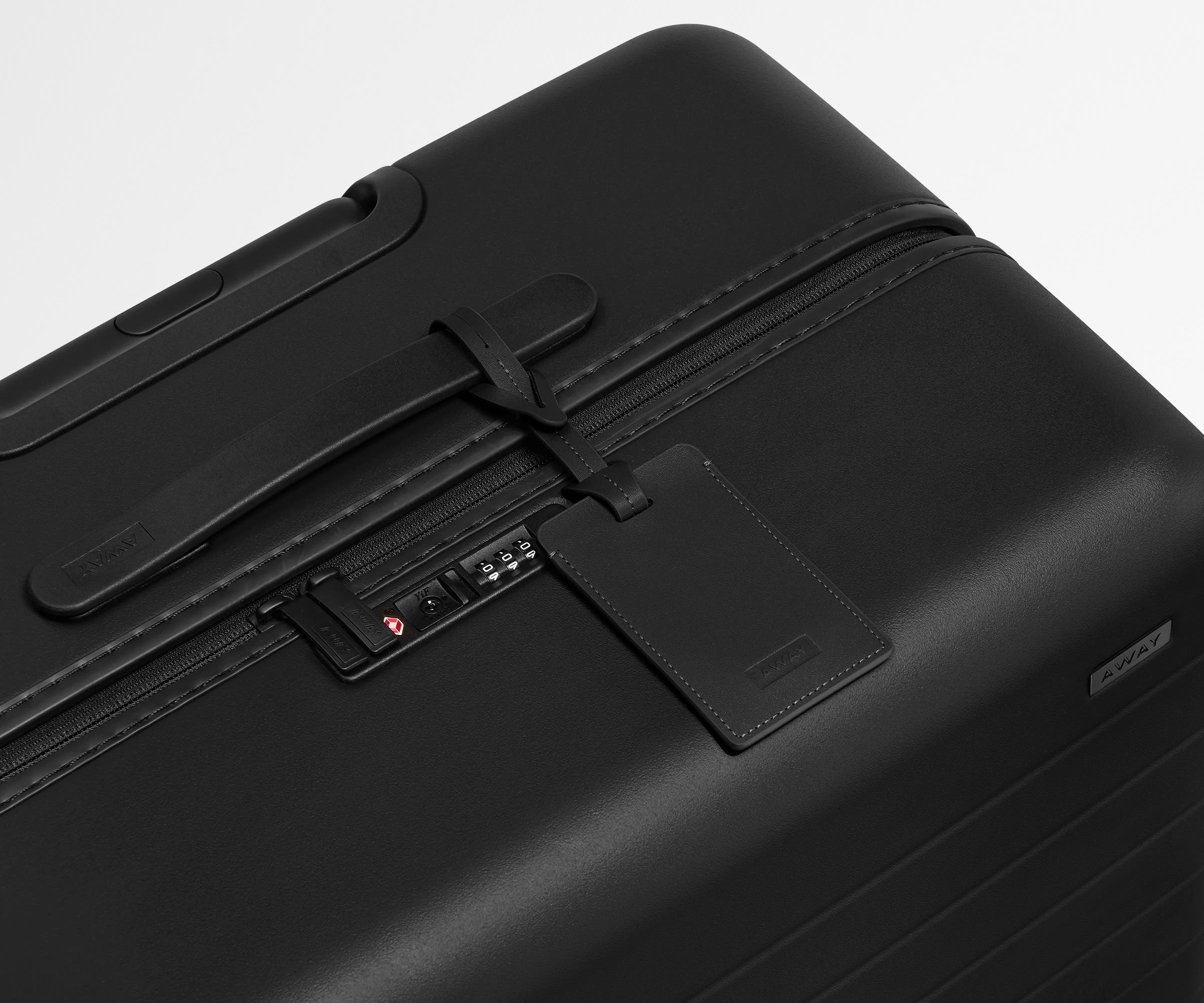 The Medium suitcase in Jet Black shown shown from above highlighting TSA-approved combination lock and recycled leather luggage tag